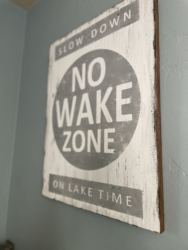 white and gray wood wall sign with phrase "slow down no wake zone on lake time adds to coastal aesthetics of bathroom