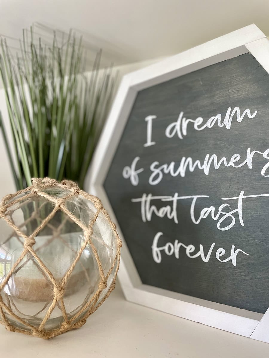 Shelf decor including green grasses, glass sphere and sign that says "I dream of summers that last forever"