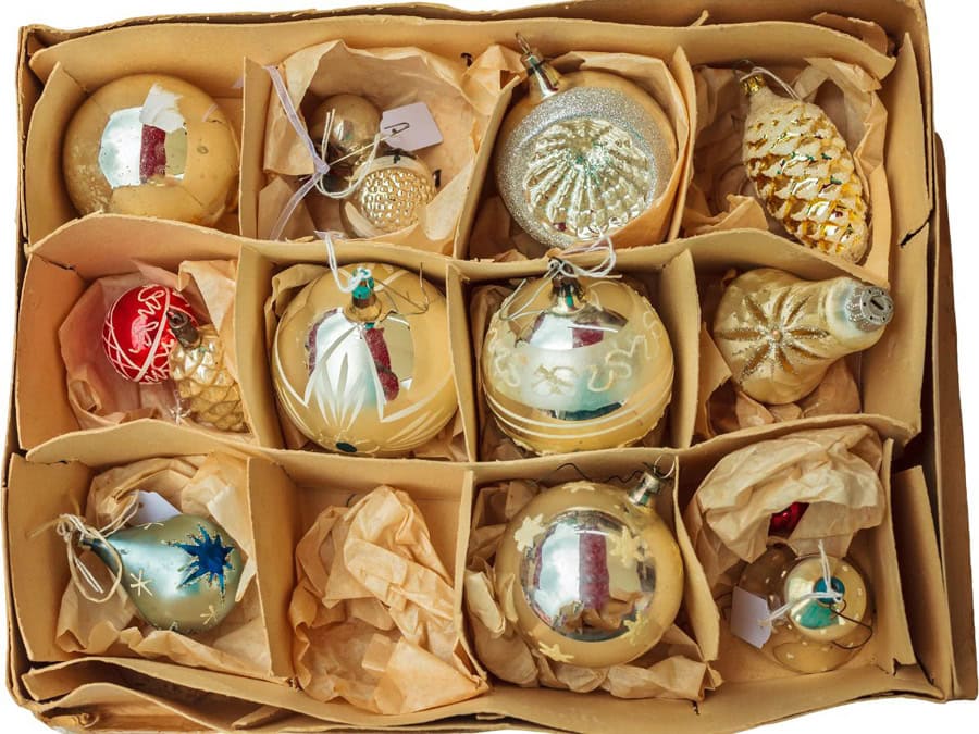 Cardboard box with divided sections holding fragile Christmas ornaments, wrapped in paper for safe storage.