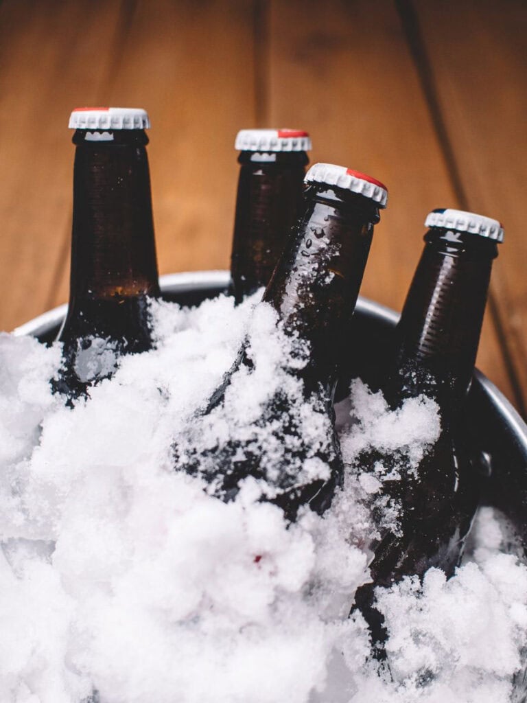 Bottles of beer nestled in a galvanized tub filled with fresh snow, creating a rustic and festive cooling solution for your cocktail station.