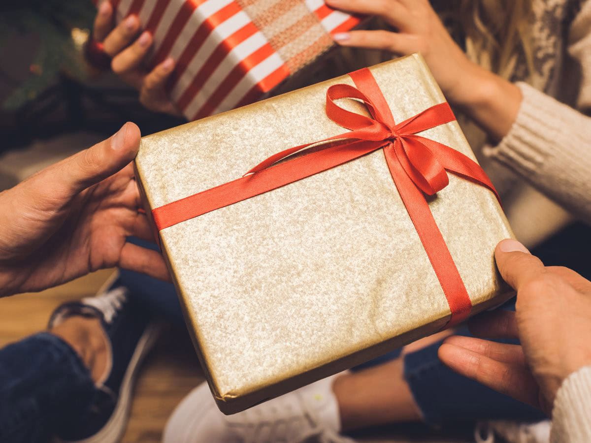 Hands exchanging a beautifully wrapped gift in gold paper with a red ribbon, perfect for a theme Christmas gift exchange.
