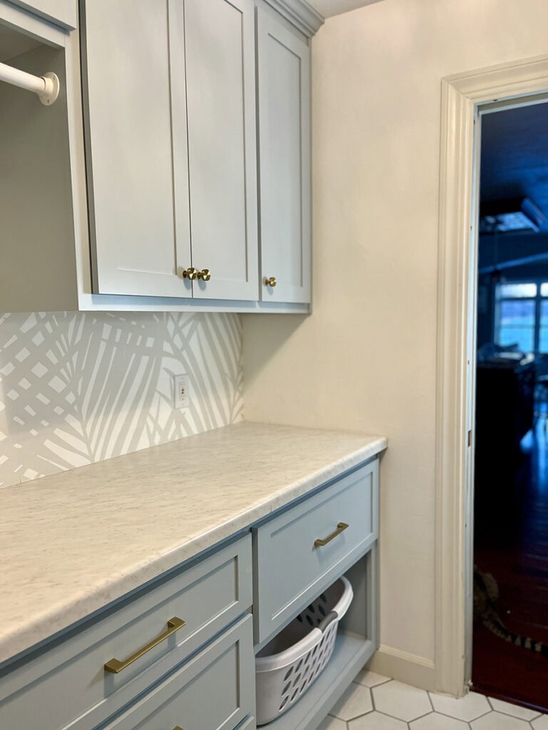 Marble-look laminate countertops paired with Niebla Azul blue cabinet paint in a coastal-inspired laundry room. A budget-friendly alternative to real marble that complements coastal blue cabinets beautifully.