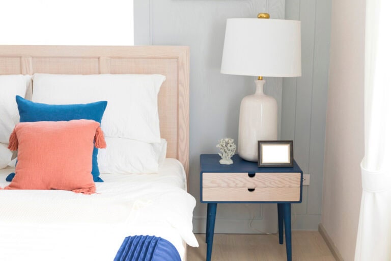 A spring home bedroom refresh featuring a coastal-inspired nightstand, a chic ceramic lamp, and vibrant throw pillows for a fresh seasonal update.