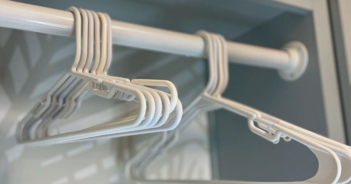 White plastic hangers neatly arranged on a drying rod, mounted under a soft blue Shaker-style cabinet in a freshly updated laundry room. The subtle palm-leaf wallpaper in the background adds a light coastal touch.