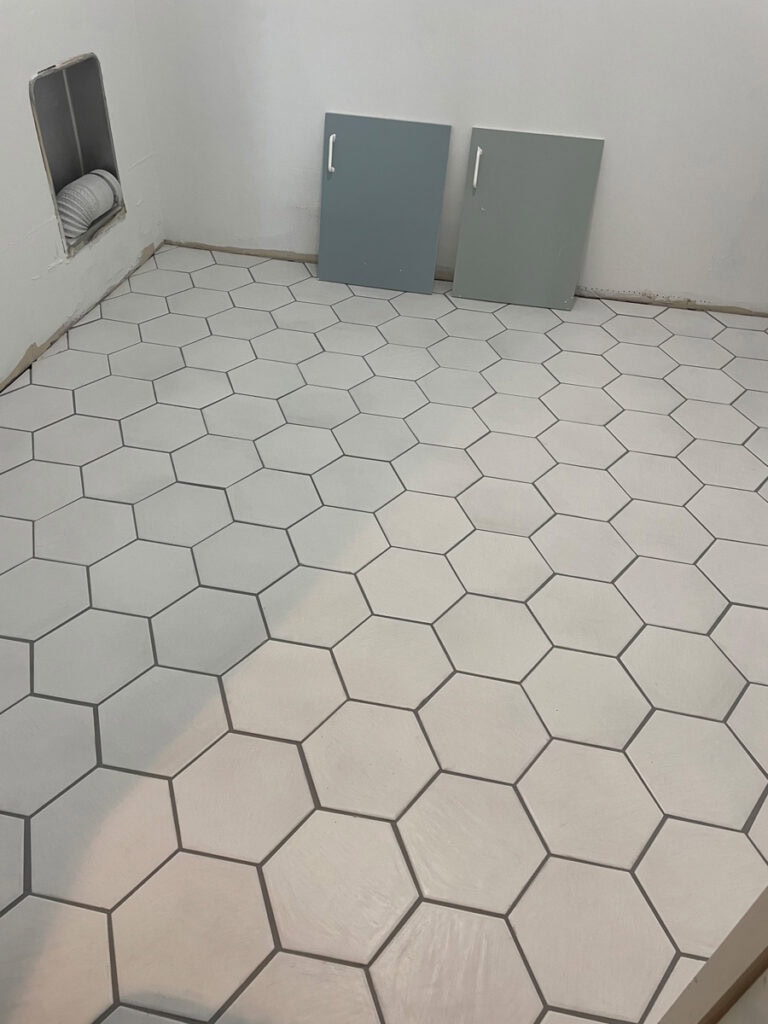 Completed white hex tile floor with charcoal grout, featuring two blue cabinet samples for a laundry room makeover.