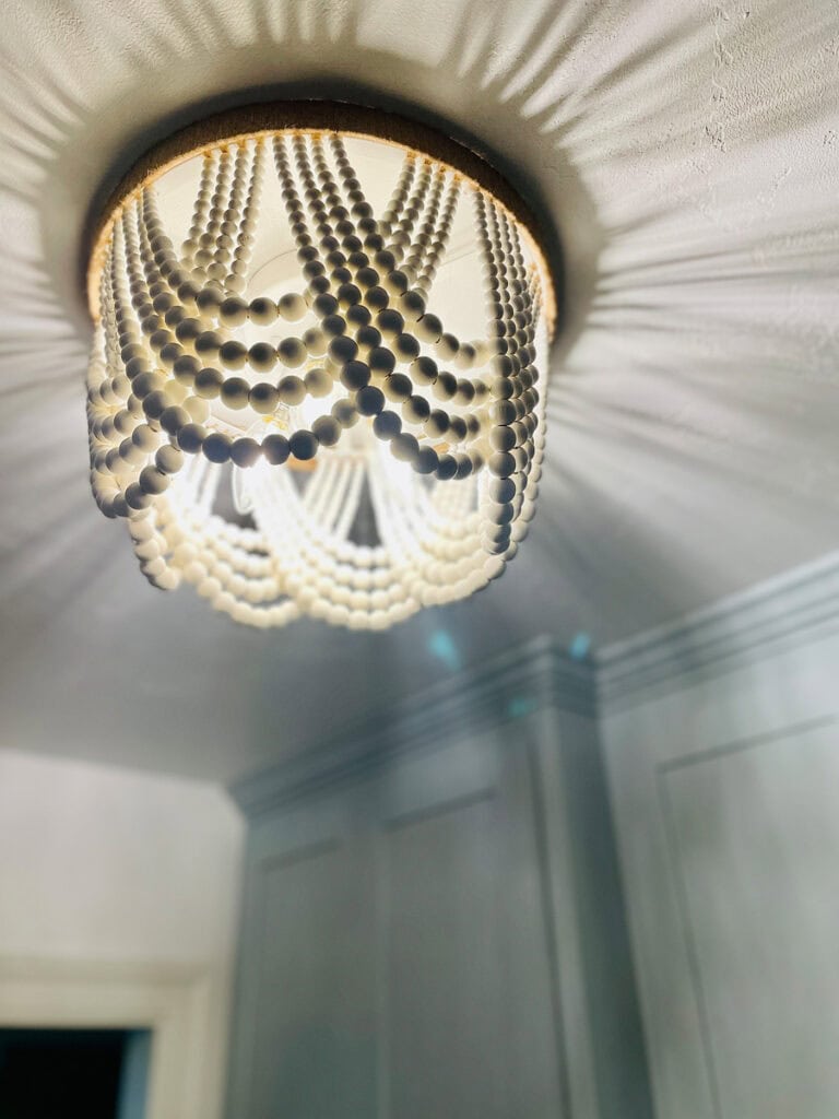 Close-up of a wood-beaded flush mount ceiling light casting soft shadows in a coastal-inspired laundry room makeover.