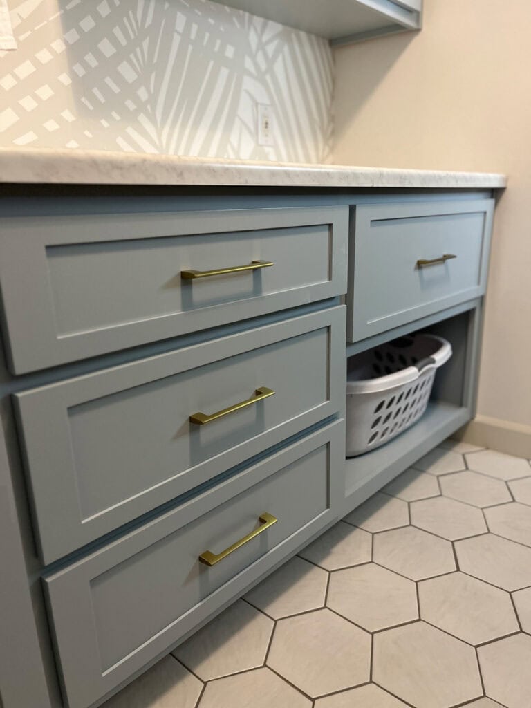 Custom deep, wide drawers in a Niebla Azul coastal laundry room makeover with gold hardware and hidden laundry basket storage.