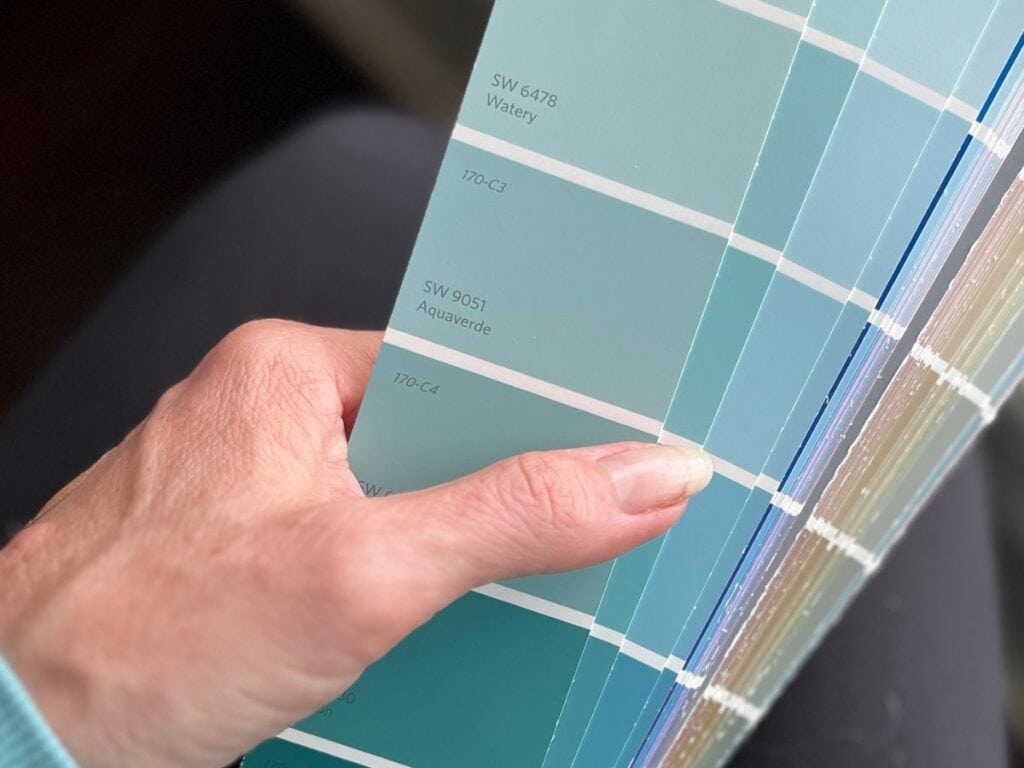 Close-up of a hand holding a Sherwin-Williams paint fan deck showing Aquaverde SW 9051 next to Watery SW 6478