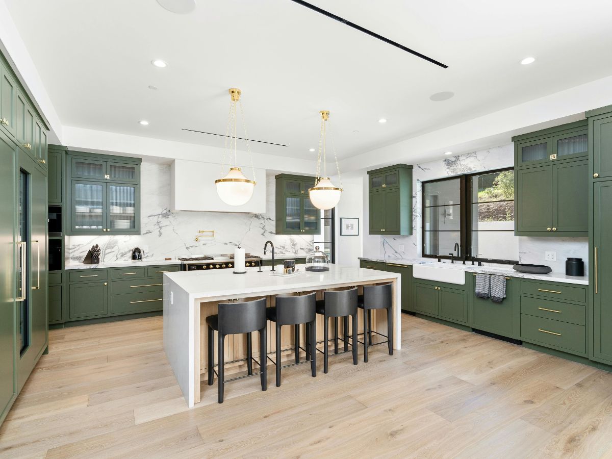 Kitchen with dark green painted cabinets, gold hardware, and a large white island with wood accents.