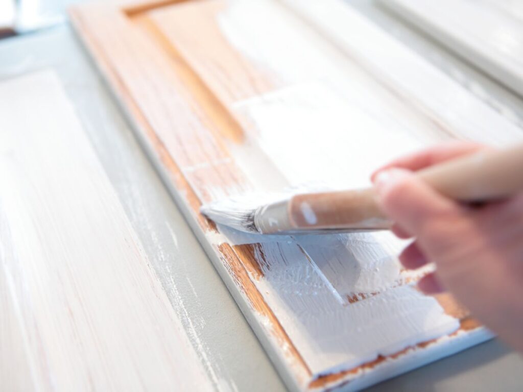 Brushing white paint on a cabinet door during a budget-friendly cabinet update.