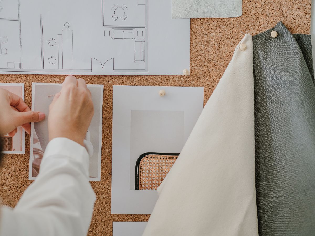 Hands creating a mood board with fabric swatches, floor plan sketches, and decor photos for coastal home styling.