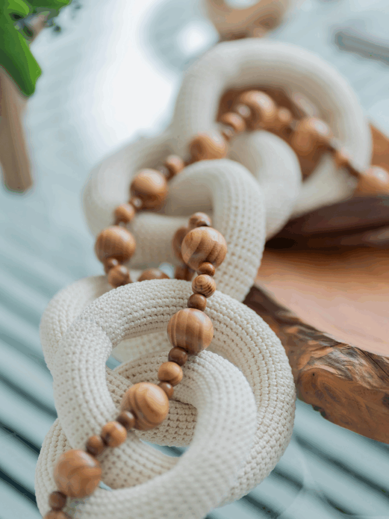 A soft cream-colored knit garland with natural wood beads, layered on a wood accent tray over glass.