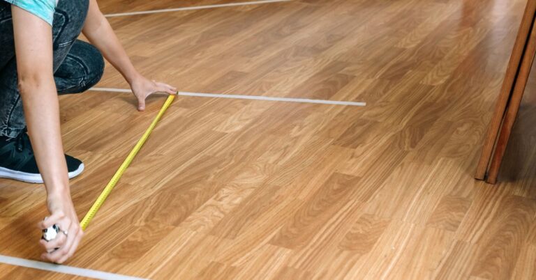 Person using a measuring tape and white painter’s tape to mark furniture layout on a wood floor