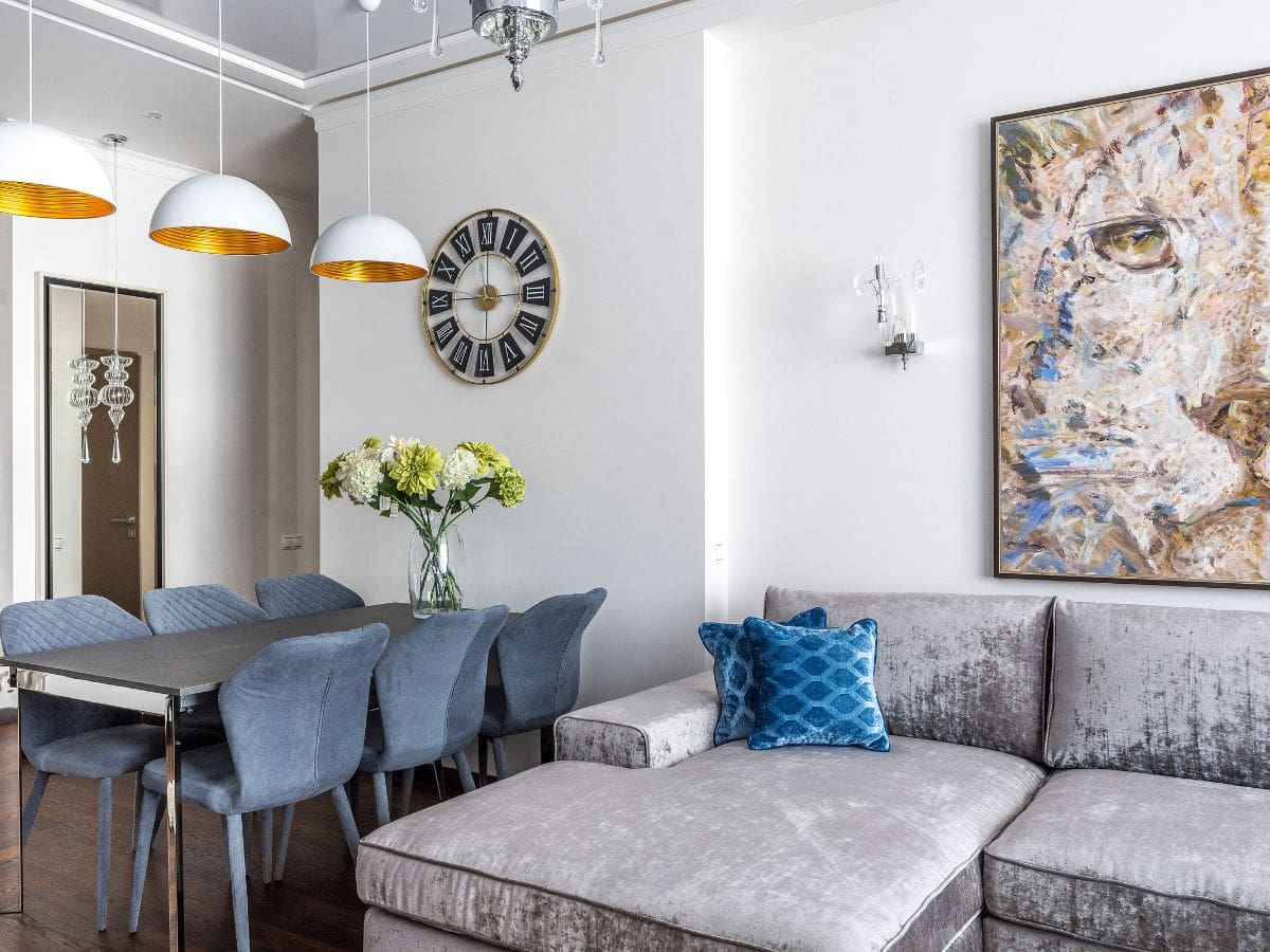 Blue accent pillow on a neutral sofa echoes color from abstract wall art—showing how small pops can tie into your interior paint color palette.