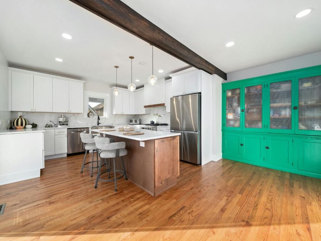 Kitchen with bold green hutch, white cabinets, and wood flooring