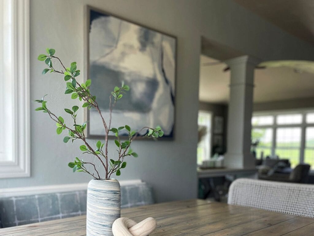 Ocean-inspired abstract artwork with green sprig in marbled vase on wood table – inspiration for coastal interior paint colors