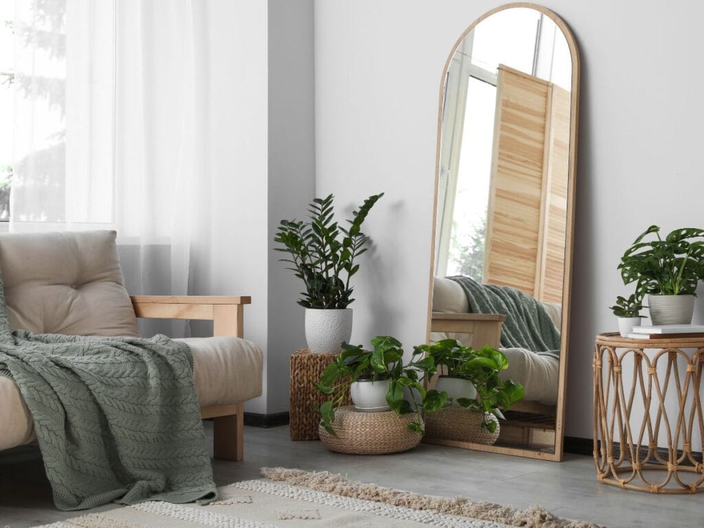 Tall arched mirror in a light, cozy room with natural wood, plants, and soft green textiles—showing how mirrors can brighten dim corners and improve interior paint color perception.
