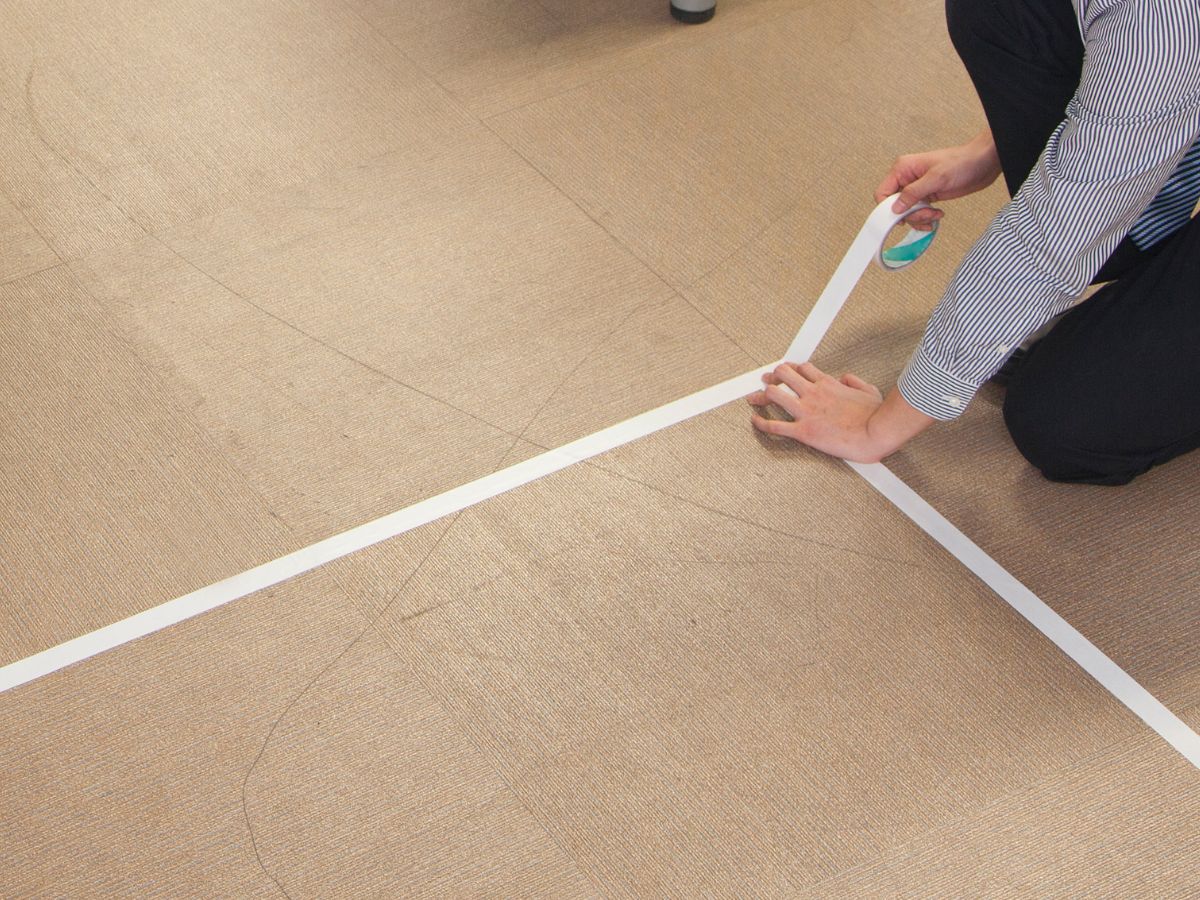 Person marking floor with painter’s tape to mock up kitchen layout during renovation planning.