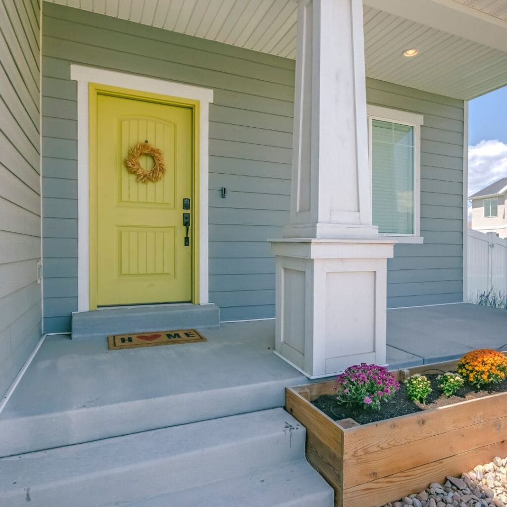 Lemon yellow painted front door on a coastal home exterior for lemon home decor inspiration and summery curb appeal.