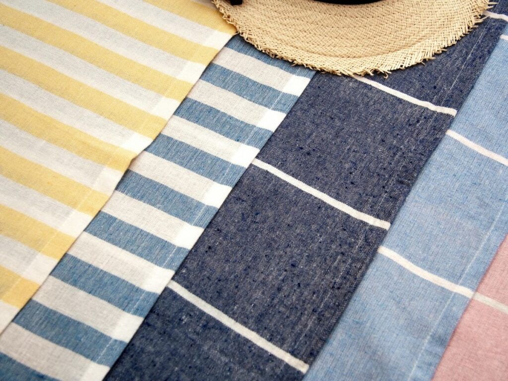 Folded Turkish beach towels in lemon yellow, coastal blue, and navy stripes, with a woven sun hat on top, perfect for coastal lemon decor outdoors.