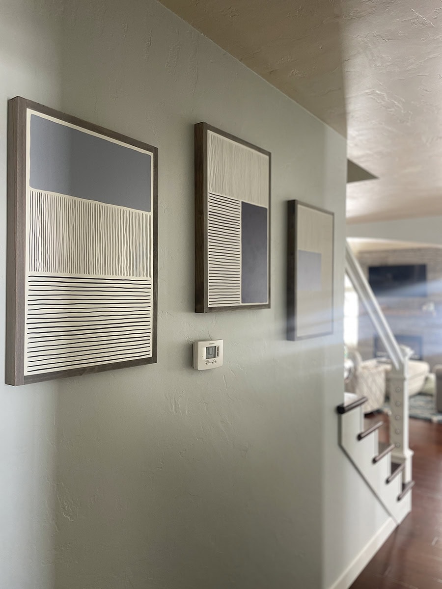 Hallway painted in SW Silver Strand with modern abstract art, showing how this chameleon paint color shifts to misty gray in low light