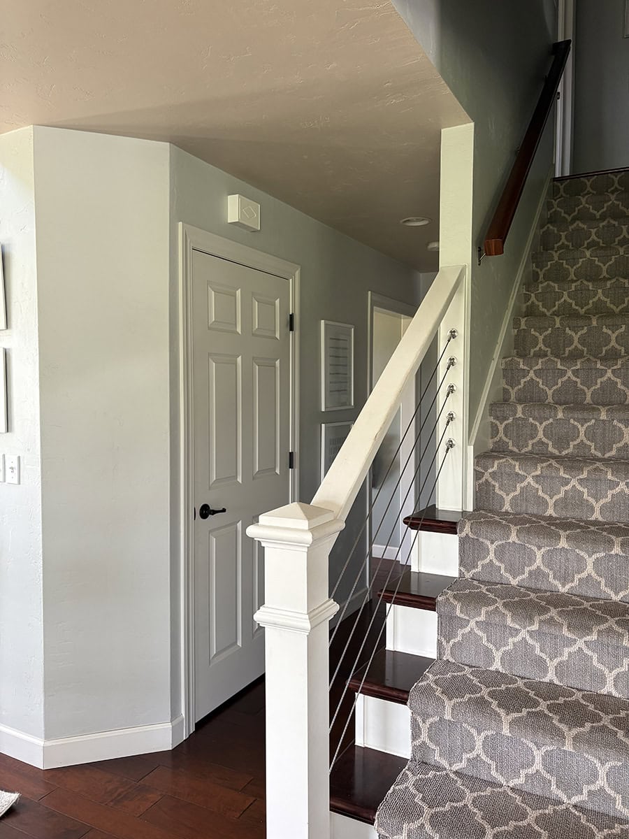Staircase and hallway painted in SW Silver Strand with Pure White trim, dark wood floors, and patterned carpet runner