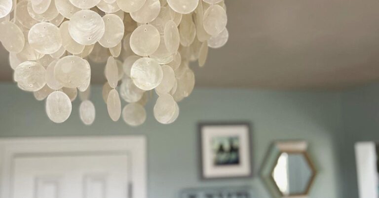 Round capiz flush mount coastal lighting fixture against a soft blue wall with white trim, adding shimmer and airy coastal style.