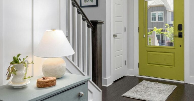 Entryway with crisp white trim, green front door, and staircase with dark wood railing — showcasing the best white paint for trim.