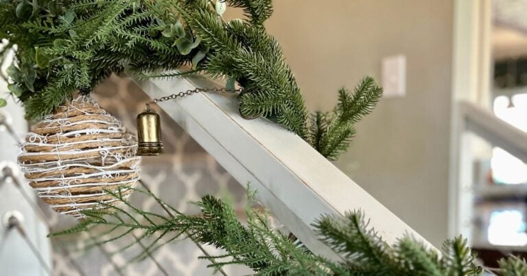 Coastal Christmas staircase garland with natural greenery, a rope-wrapped ornament, and a brass bell, adding holiday cheer to the stairs.