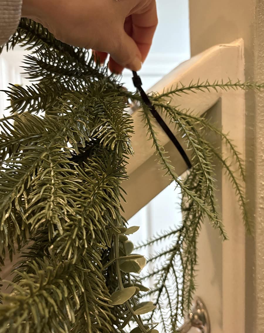 Hand using zip tie to secure garland to the staircase railing.