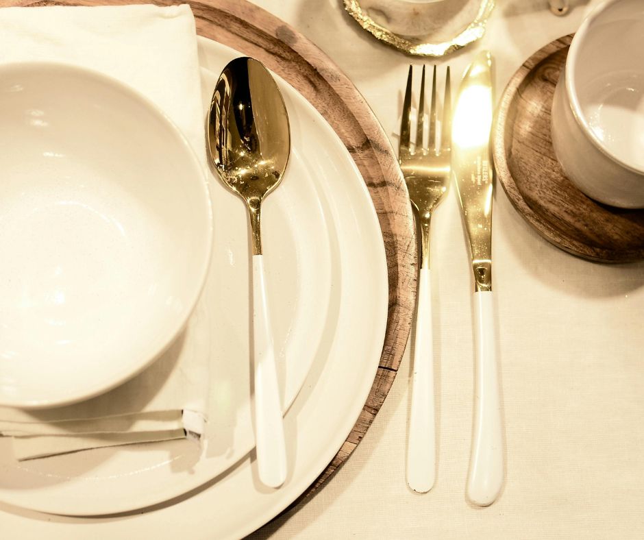 Gold flatware and white dinnerware layered on a wooden Thanksgiving table with subtle holiday shimmer.