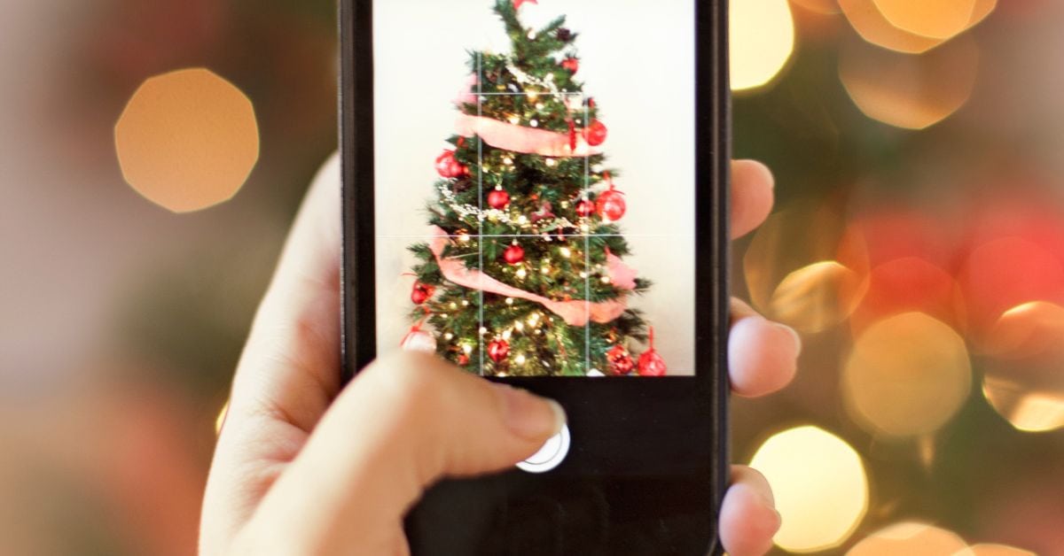Person taking a photo of a decorated Christmas tree with red ornaments and ribbon to remember holiday decorating ideas for next year.