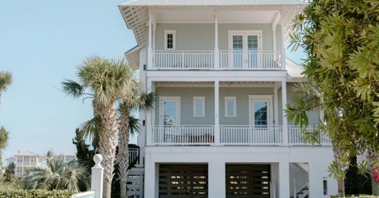 Light blue beach house exterior with white trim, palm trees, and double porches — a clean example of coastal exterior paint colors for calm, timeless curb appeal.