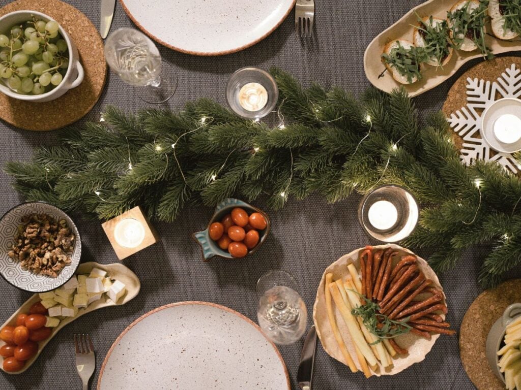Holiday hosting snack table with twinkle-lit garland, candles, and simple appetizer bowls set for guests