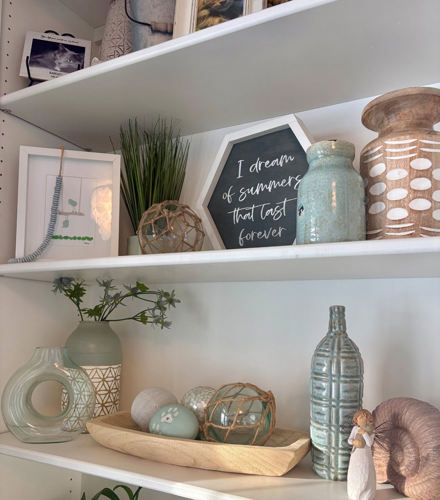 (CAPTION) After removing deep teal accents and colorful book spines, this shelf relies on soft aqua, beachy wood, and fresh white to support meaningful pieces.