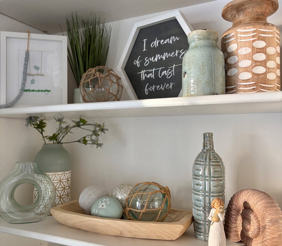 Shelf decor styled with soft aqua glass, natural wood accents, and meaningful decor on white built-in shelves.