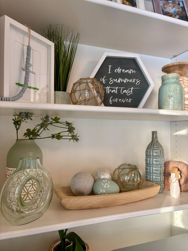 Shelf decor styled with a limited coastal color palette, showing soft aqua glass, neutral textures, and fewer competing colors on white shelves.