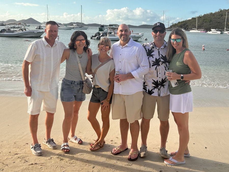 Group photo at Cruz Bay, St. John, showcasing warm coastal tones of the shore and vibrant, fun outfits that match the Shoreline Mist color palette.