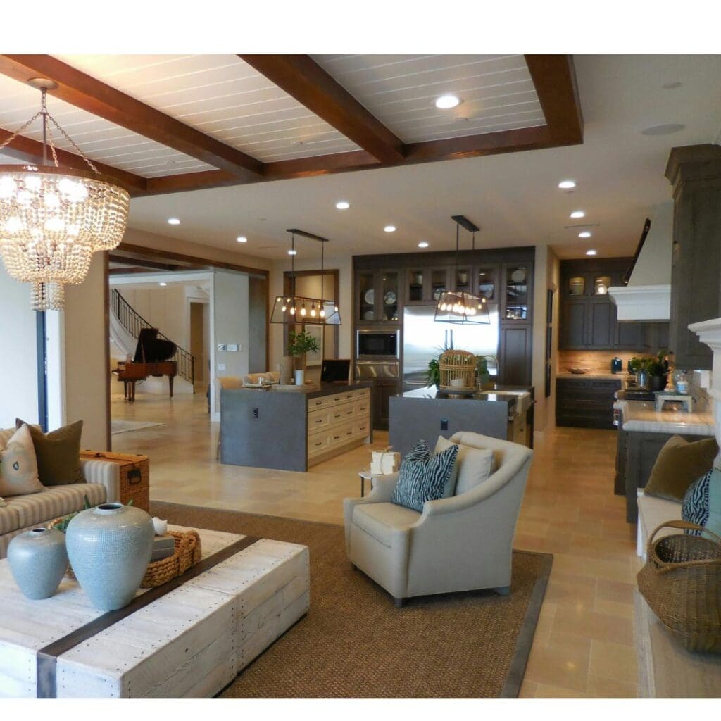 A spacious living room and open kitchen, featuring neutral walls and coastal-inspired accents like pillows and decor that link the two spaces.