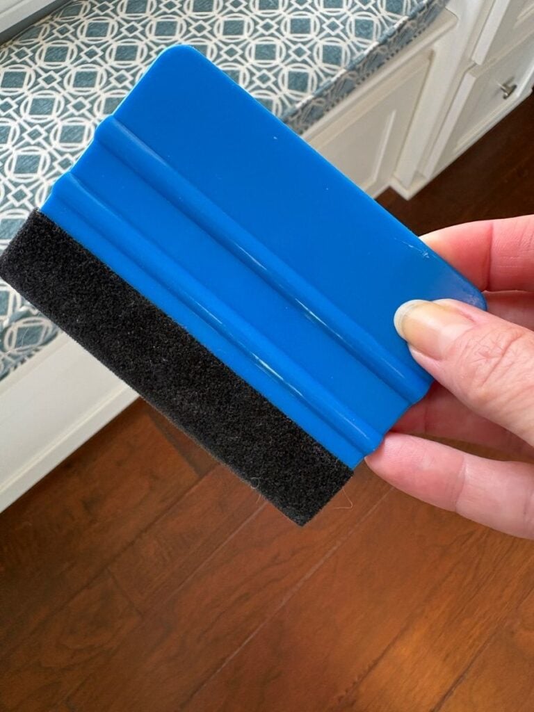 A wallpaper smoothing tool with soft felt, used for applying wallpaper, resting on a wooden surface with the wallpaper in the background.