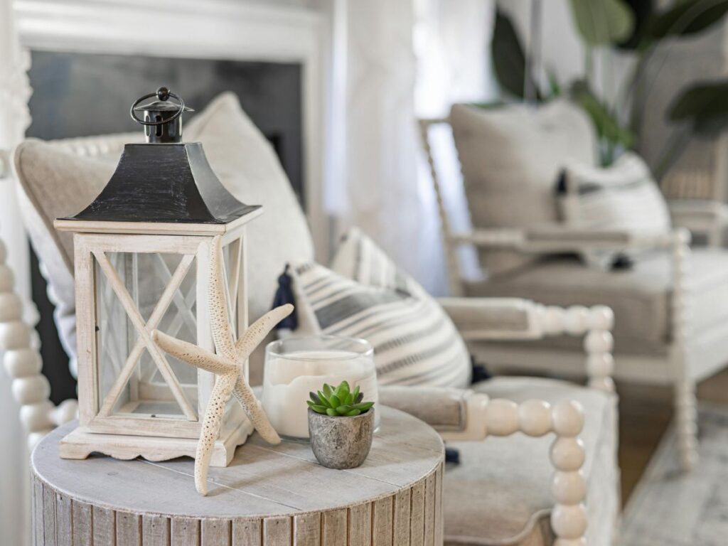 Coastal living room with a soft gray sofa, neutral pillows, a textured throw, a round wooden side table, and decorative accents including a starfish, candle, and small plant, showing layered tones and textures that create a cohesive, inviting space.