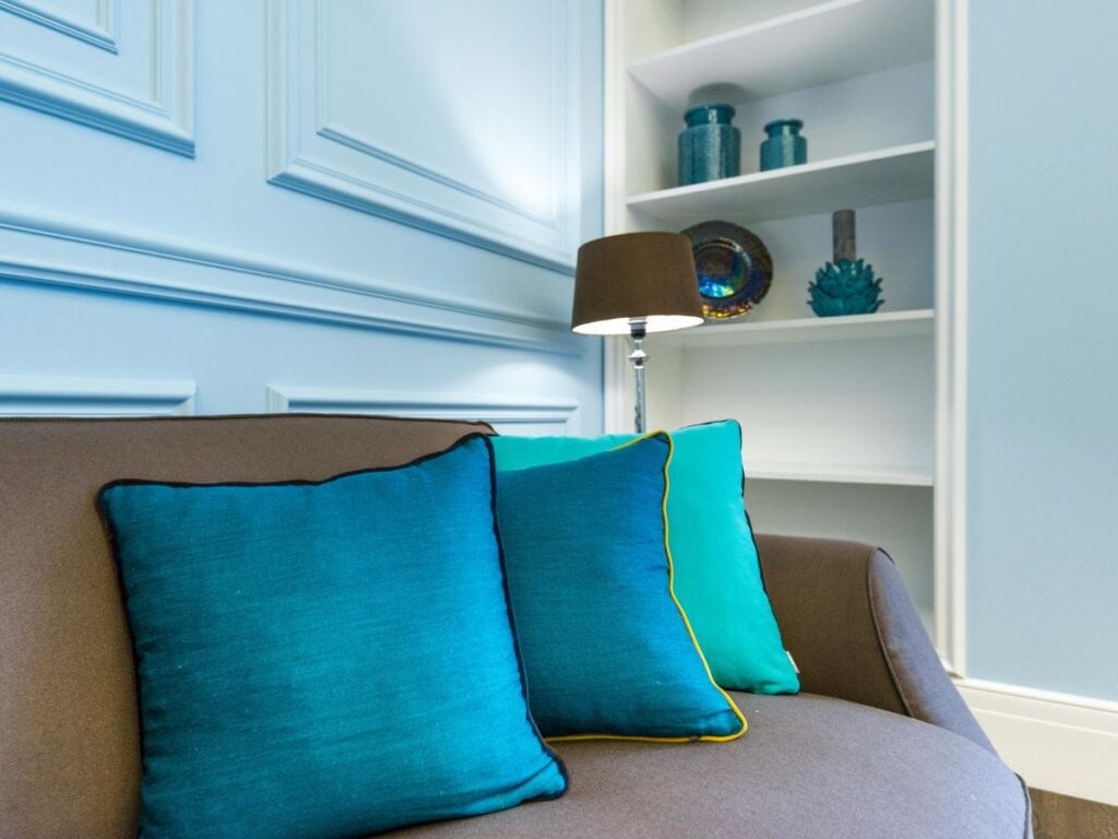 Close-up of a gray couch with three pillows in varying aqua tones, arranged from light to dark, demonstrating tonal layering for depth and visual interest.