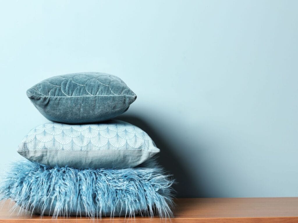Stacked blue pillows showing how to decorate with tonal layering in coastal style, using light, medium, and dark shades for effortless flow