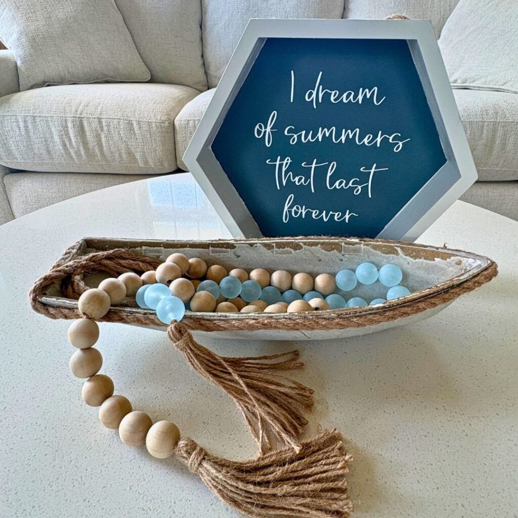 Lake house decor inspiration featuring a handmade "I Dream of Summers That Last Forever" sign styled with coastal decor, a decorative boat, and wood bead garland.
