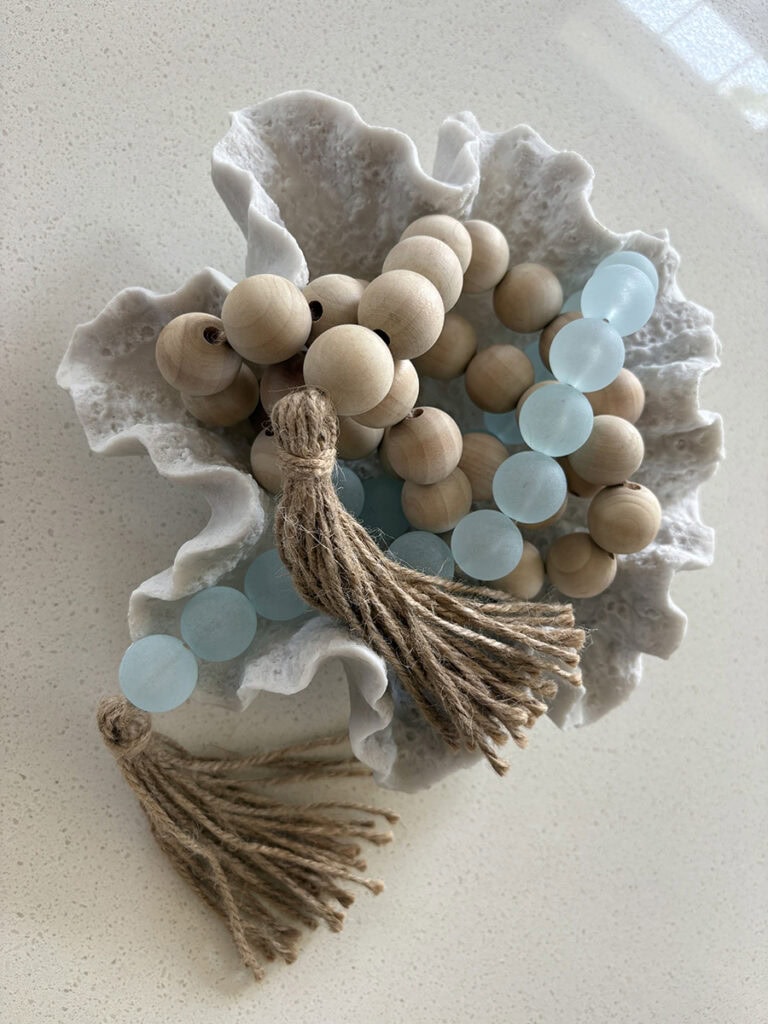 Textured white coral bowl filled with a natural wood and aqua bead garland used as an anchor for coastal table decor.