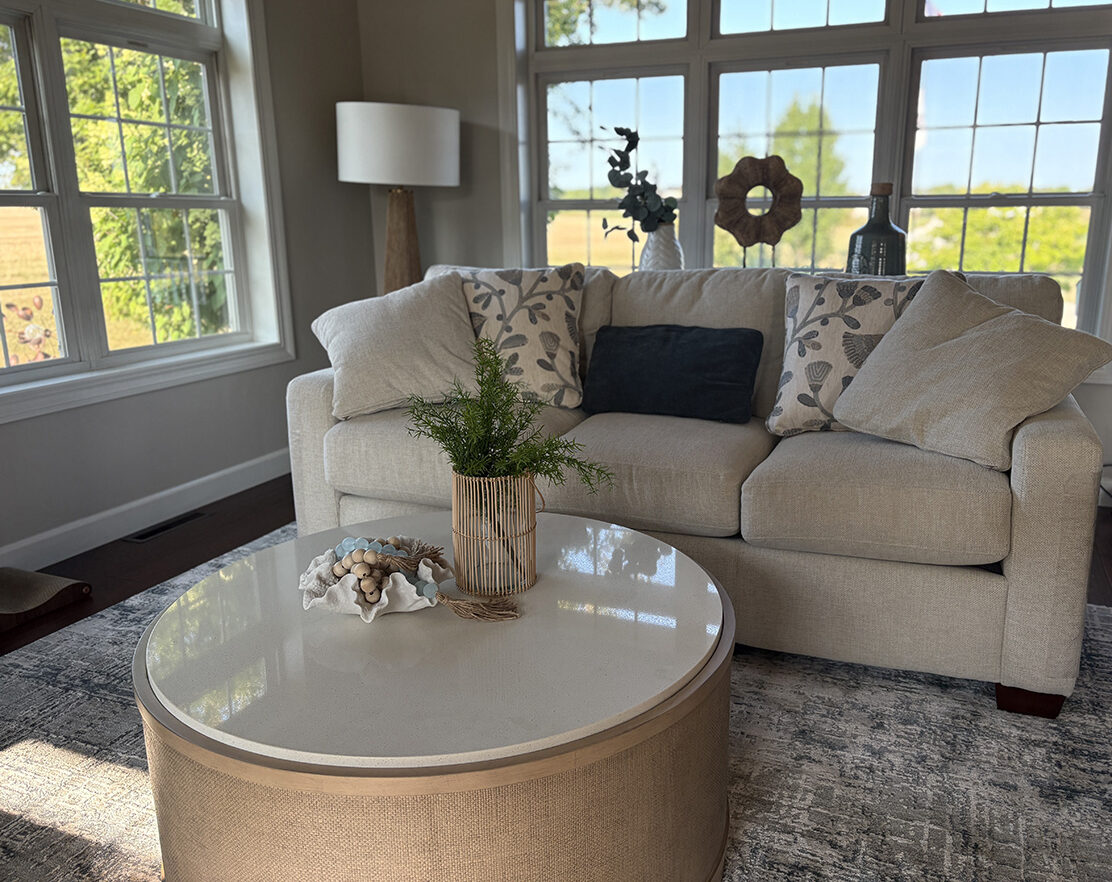Round coffee table decor ideas with a coral bowl, aqua bead garland and woven vase with greenery in a bright coastal living room.