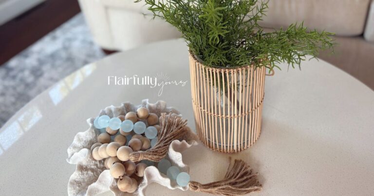 Round coffee table decor with a coral bowl, aqua and wood bead garland, woven vase and greenery in a bright coastal living room.