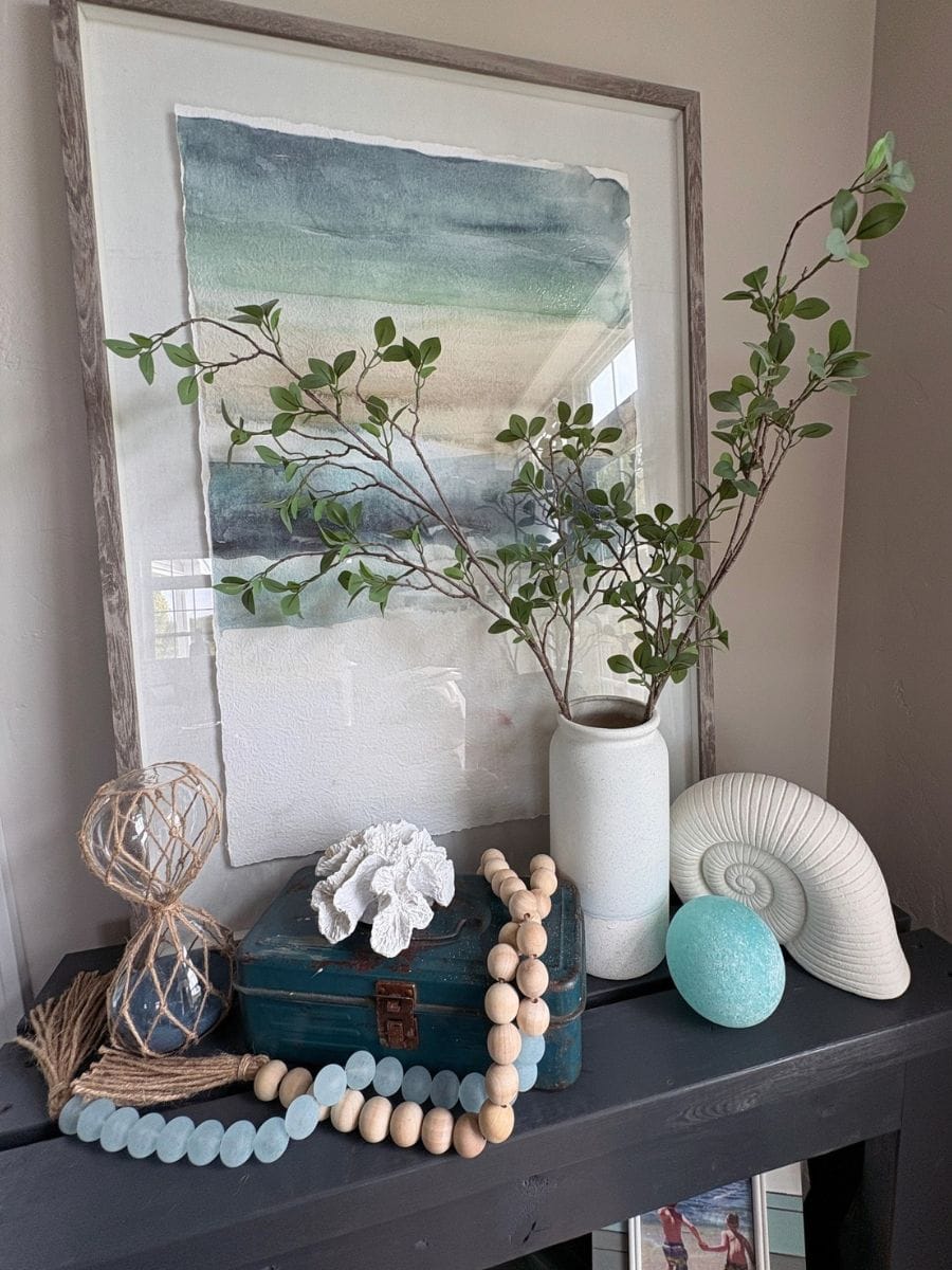 Coastal console table styled with aqua accents, white coral, nautilus shell, sea glass beads and greenery