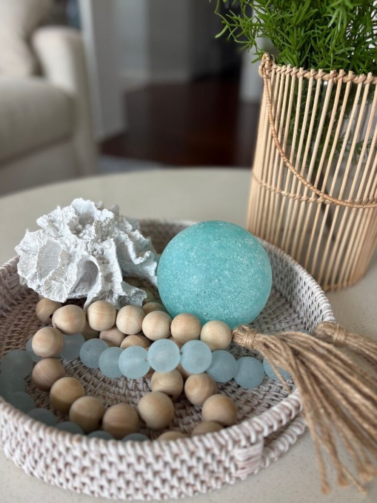 Aqua and natural wood decorative beads styled in a coral bowl with greenery and a woven vase on a coffee table.