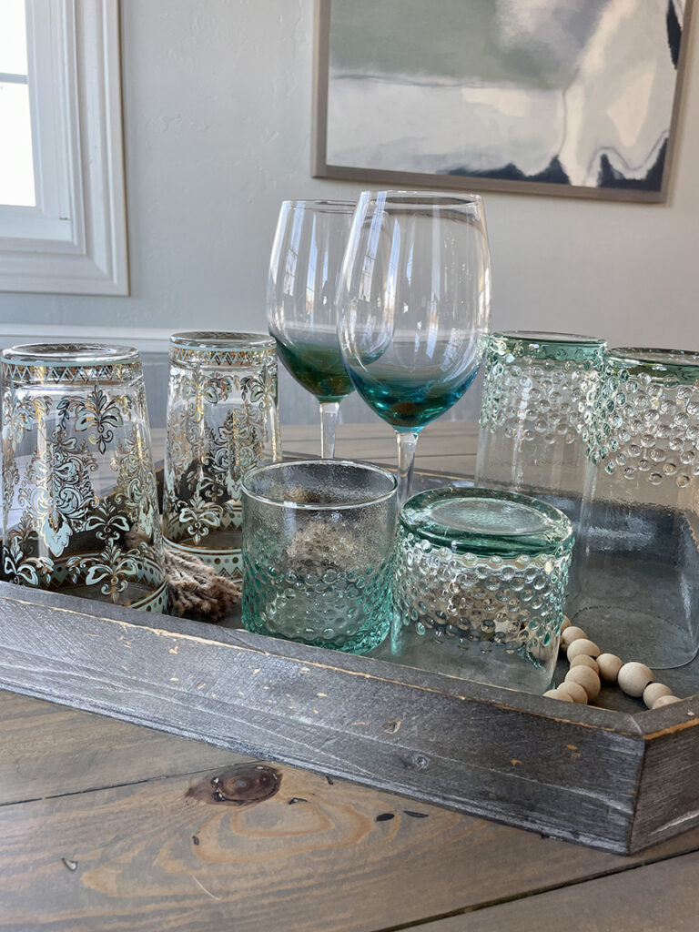 Mix of aqua, clear and patterned glassware displayed on a wood tray for entertaining guests.